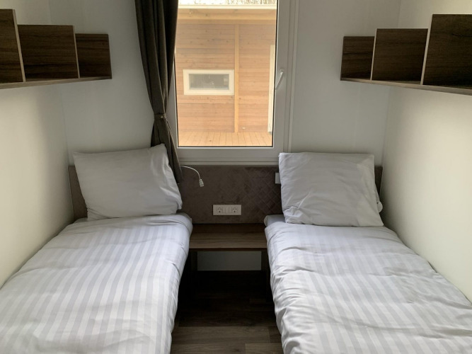 Foto van een eenvoudige lodgekamer met twee eenpersoonsbedden, witte lakens, planken en een raam.