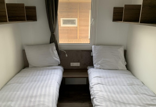 Fotografi af et simpelt lodgeværelse med to enkeltsenge, hvide lagner, hylder og vindue mod trævæg.