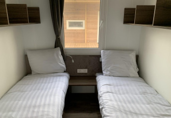 Afbeelding van een simpele lodgekamer met twee enkele bedden, witte lakens, planken en een raam.