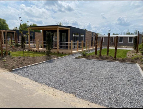 Moderne hytte ved Zuiderzee i Holland med grusstier, grønne græsplæner og træterrasse i solskin.