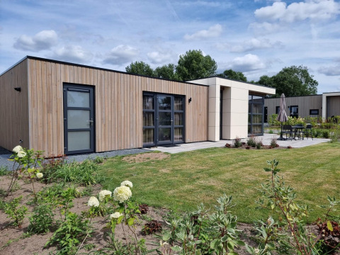 Cube Maximaal 4 lodge featuring a modern wooden exterior, large windows, and a spacious garden area.