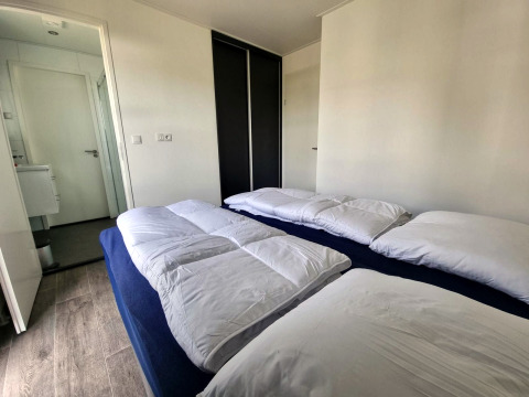 Modern bedroom at Cube Maximaal 4 lodge at Zuiderzee in the Netherlands, featuring two beds and white duvets.