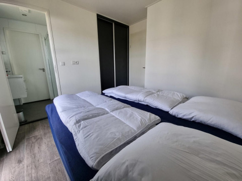 Moderne slaapkamer in Cube Maximaal 4 lodge bij Zuiderzee, Nederland, met twee bedden en witte dekbedden.