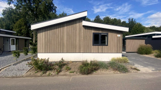 Lodge Hackfort MIVA moderne avec façade en bois, toit incliné et verdure par une journée ensoleillée.
