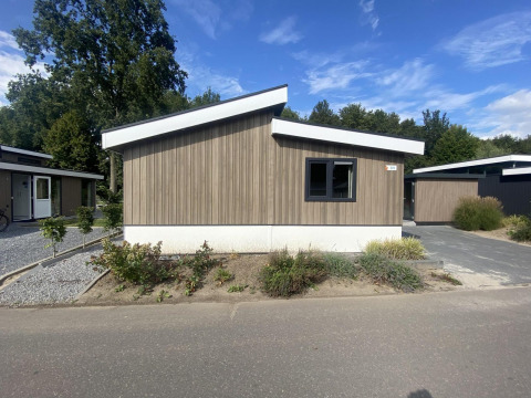 Moderne Hackfort MIVA-lodge met houten gevel, schuin dak en beplanting op een zonnige dag.