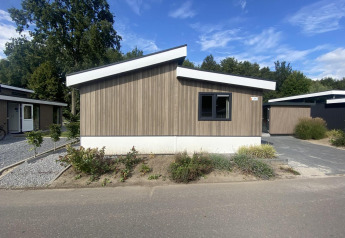 Moderne Hackfort MIVA-lodge med træfacade og hældende tag på en solrig dag omgivet af grøn beplantning.