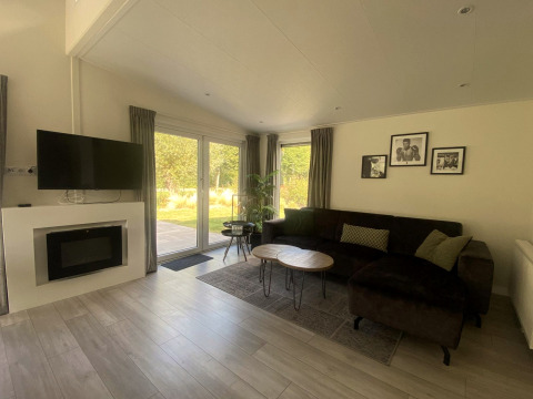 Sala de estar del lodge Hackfort MIVA en Zuiderzee, Países Bajos, con sofá, televisor y ventanales al jardín.