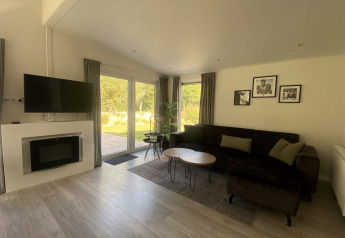 Woonkamer van Hackfort MIVA-lodge aan het Zuiderzee in Nederland met bank, tv en uitzicht op tuin.