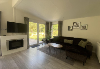 Stue i Hackfort MIVA-lodgen ved Zuiderzee i Holland med moderne sofa, tv og store vinduer til haven.