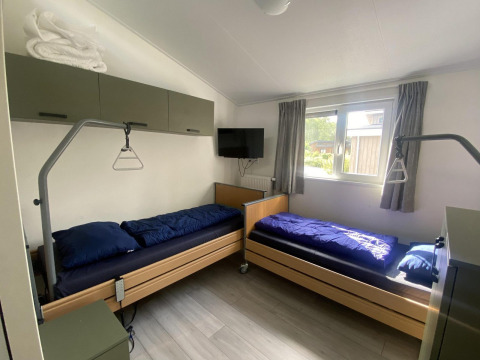 Twee enkele bedden met blauw dekbed in een heldere kamer van Hackfort MIVA lodge, Zuiderzee, Nederland.