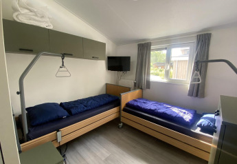 Two single beds with blue bedding in a bright room at Hackfort MIVA lodge, Zuiderzee, Netherlands.