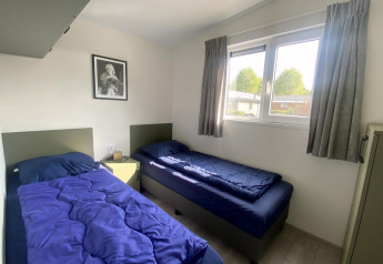 Twee eenpersoonsbedden met blauwe dekens in de Hackfort MIVA-lodge bij Zuiderzee, Nederland.