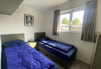 Two single beds with blue bedding in a bright room at Hackfort MIVA lodge at Zuiderzee, Netherlands.