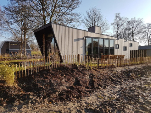 Modernes Tiny House namens Just Nature 4, umgeben von Natur, Holzzaun und kahlen Bäumen im Sonnenlicht.