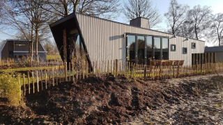 Casa tiny moderna chiamata Just Nature 4, circondata da natura, staccionata in legno e alberi spogli.
