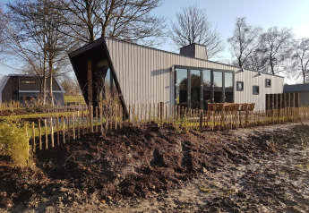 Moderne tiny house Just Nature 4, omgeven door natuur, houten omheining en kale bomen bij daglicht.