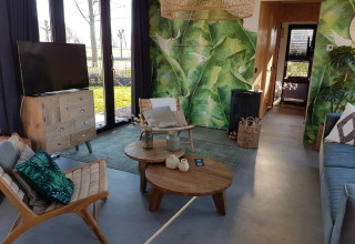 Soggiorno di una tiny house con parete verde, mobili in legno e grandi finestre a Just Nature 4, Zuiderzee, Paesi Bassi.