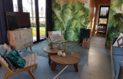 Wohnzimmer eines Tiny Houses mit Pflanzenwand, Holzmöbeln und großen Fenstern in Just Nature 4, Zuiderzee, Niederlande.