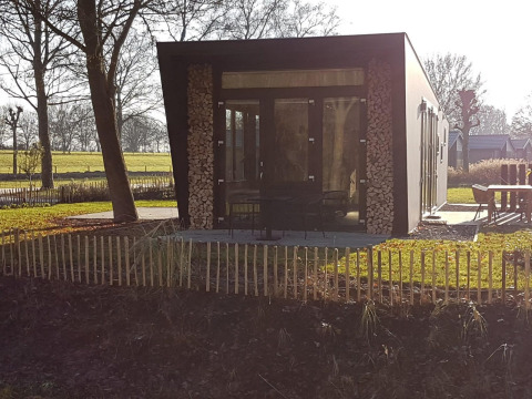 Tiny house Just Nature 4 aan Zuiderzee in Nederland, met gestapeld hout en een moderne glazen gevel.