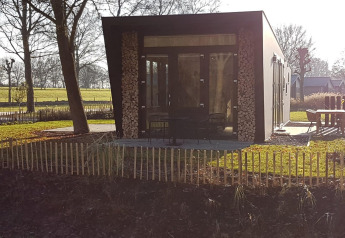 Tiny house Just Nature 4 aan Zuiderzee in Nederland, met gestapeld hout en een moderne glazen gevel.