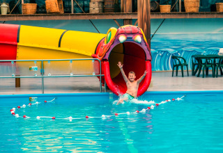 Junge rutscht fröhlich eine bunte Wasserrutsche in Form eines Tieres im Glamping-Unterkunftspool hinunter.