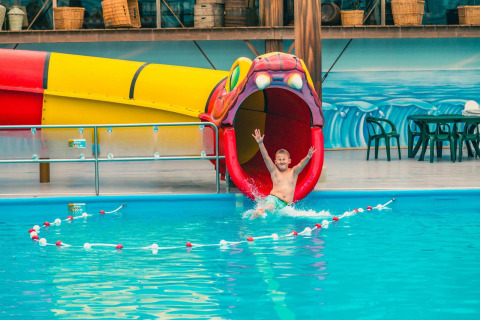Junge rutscht fröhlich eine bunte Wasserrutsche in Form eines Tieres im Glamping-Unterkunftspool hinunter.