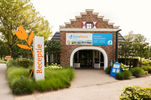 Eingang zur EuroParcs Glamping-Rezeption mit Tulpen-Schild, umgeben von grüner Bepflanzung.