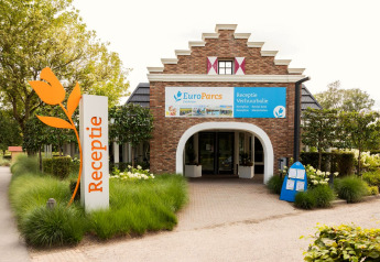Entrée de la réception d'hébergement glamping EuroParcs avec panneau tulipe, entourée de verdure.