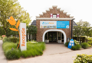 Ingang van de EuroParcs glamping-receptie met tulpenschild, omgeven door groene planten en bomen.