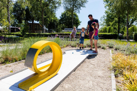 Familie spielt Minigolf im Freien auf einem modernen Glampingplatz, umgeben von Natur und Sonne.