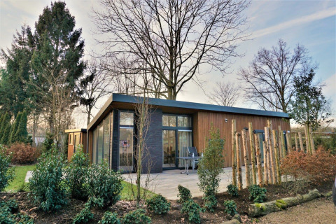 Moderne Pavillon 4 lodge med store vinduer, træfacade og frodig have under høj himmel.