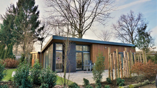 Lodge moderne Pavilion 4 avec grandes baies vitrées, façade bois et jardin verdoyant, arbres autour.