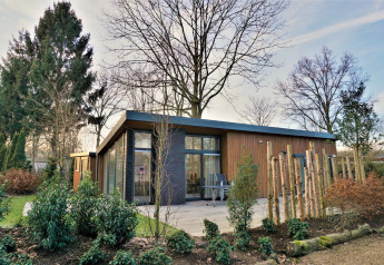 Lodge moderne Pavilion 4 avec grandes baies vitrées, façade bois et jardin verdoyant, arbres autour.