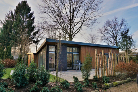 Lodge moderne Pavilion 4 avec grandes baies vitrées, façade bois et jardin verdoyant, arbres autour.