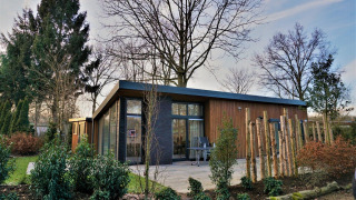 Pavillon 4, eine moderne Lodge mit Holzverkleidung, großen Fenstern und grünem Garten.