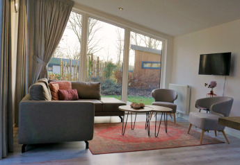 Salon moderne avec grandes fenêtres, canapé gris et vue sur jardin dans le Pavilion 4, Zuiderzee, Pays-Bas.