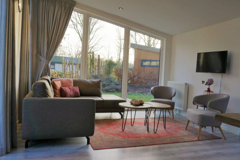 Modernes Wohnzimmer mit großen Fenstern, grauem Sofa und Gartenblick in Pavilion 4, Zuiderzee, Niederlande.
