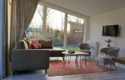 Moderne lounge med store vinduer, grå sofa og udsigt over have i Pavilion 4, Zuiderzee, Holland.