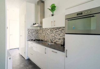 Moderne, kompakt køkken i Pavilion 4, Zuiderzee, Holland, med hvidt interiør og stilfuld mosaik-flisevæg.
