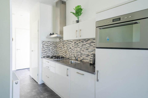 Moderne, kompakte Küche im Pavilion 4 in Zuiderzee, Niederlande, mit weißer Einrichtung und Mosaikfliesenwand.