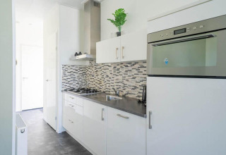 Modern, compact kitchen in Pavilion 4 at Zuiderzee, Netherlands, featuring white cabinets and mosaic tile backsplash.