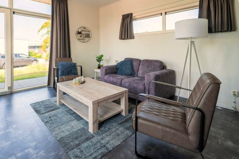 Moderne stue i Pavilion 4 ved Zuiderzee, Holland, med store vinduer, grå sofa og lænestole.