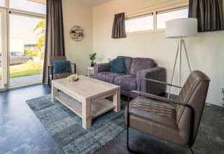Moderne stue i Pavilion 4 ved Zuiderzee, Holland, med store vinduer, grå sofa og lænestole.