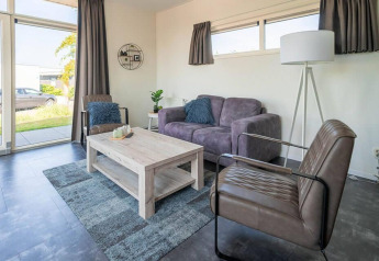 Moderne woonkamer in Pavilion 4 aan Zuiderzee, Nederland, met grijze sofa, zetels en hoge ramen.