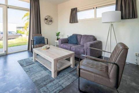 Modern living room at Pavilion 4, Zuiderzee, Netherlands, featuring a gray sofa, chairs and tall windows.