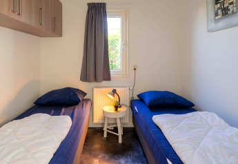 Chambre lumineuse avec deux lits simples, literie bleue et petite table au Pavilion 4, Zuiderzee, Pays-Bas.
