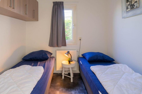 Helles Zimmer mit zwei Einzelbetten, blauer Bettwäsche und einem kleinen Tisch in Pavilion 4, Zuiderzee, Niederlande.