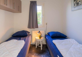 Lichte kamer met twee eenpersoonsbedden, blauw beddengoed en tafeltje in Pavilion 4, Zuiderzee, Nederland.
