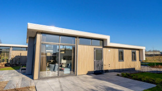 Lodge Pavilion moderne avec grandes baies vitrées, façade bois clair et terrasse par temps ensoleillé