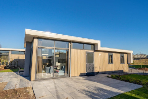 Moderne Pavilion-lodge met grote ramen, lichte houten gevel en betegeld terras onder blauwe lucht